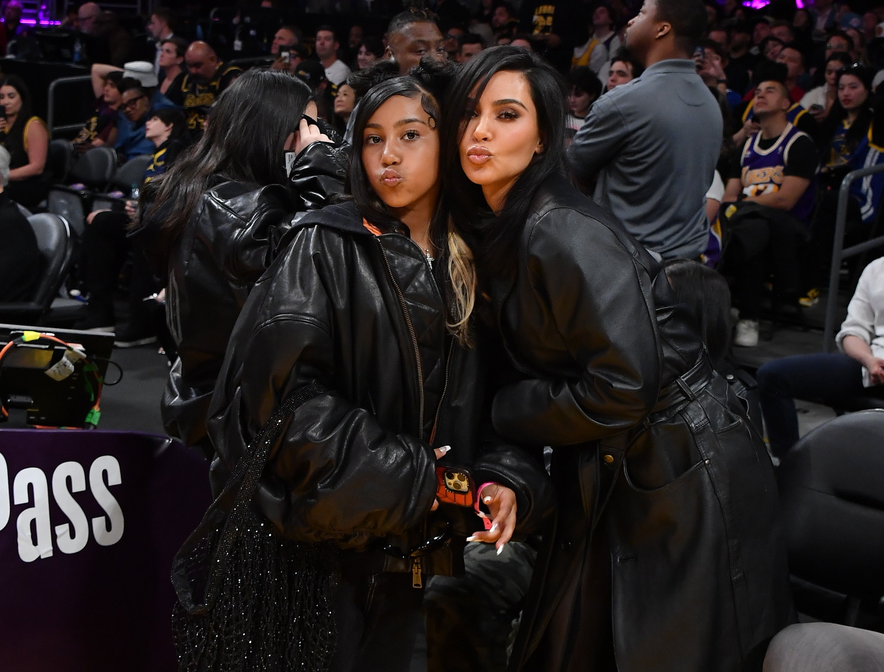 Two people pose at a sports event, both wearing stylish black leather jackets