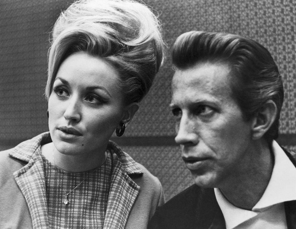 Two individuals in 1960s attire, one with an elegant updo hairstyle and the other with slicked-back hair, both appearing contemplative