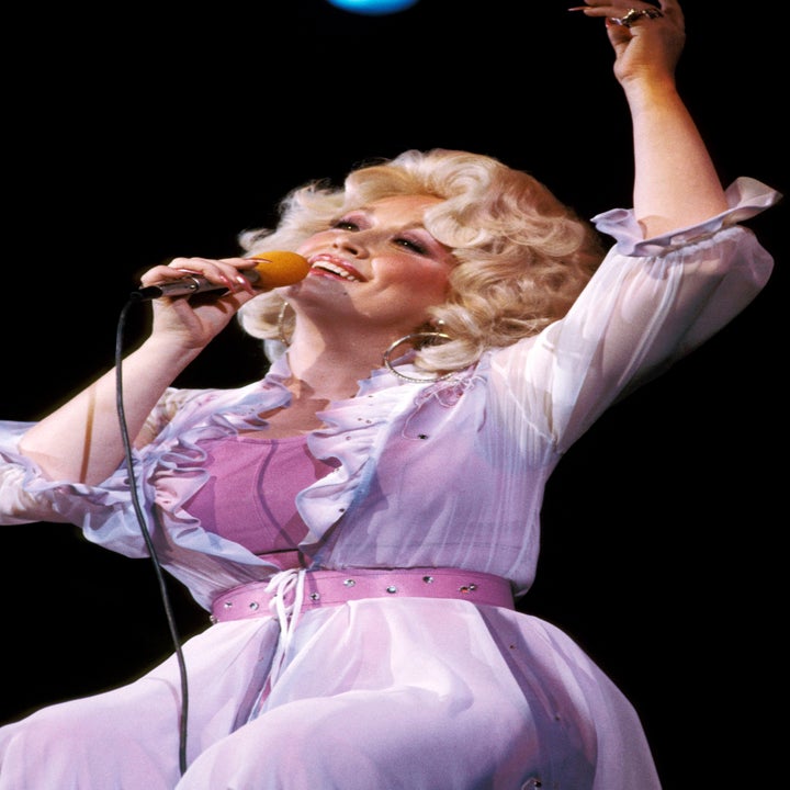 Singer on stage, wearing a frilled, sheer outfit with a wide belt, passionately singing into a microphone
