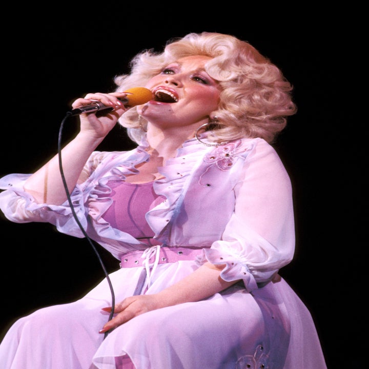 Singer performing on stage, wearing a flowing, embellished gown with sheer layers