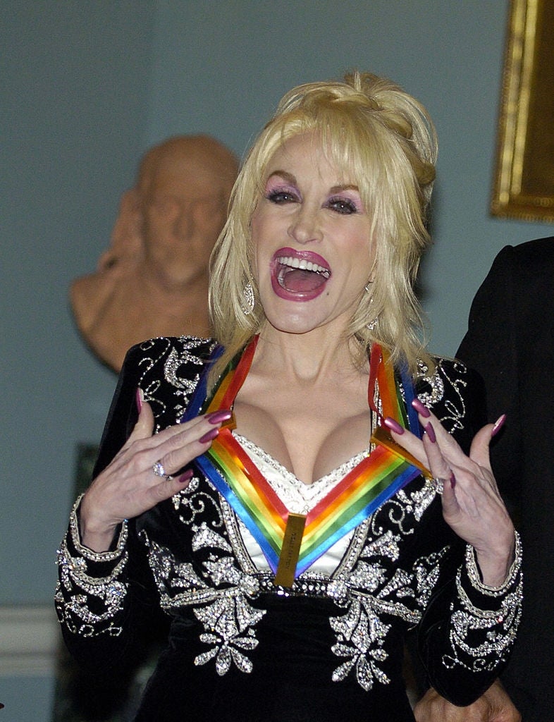 Person smiling in an embellished suit with intricate patterns, wearing a medal with a rainbow ribbon around their neck