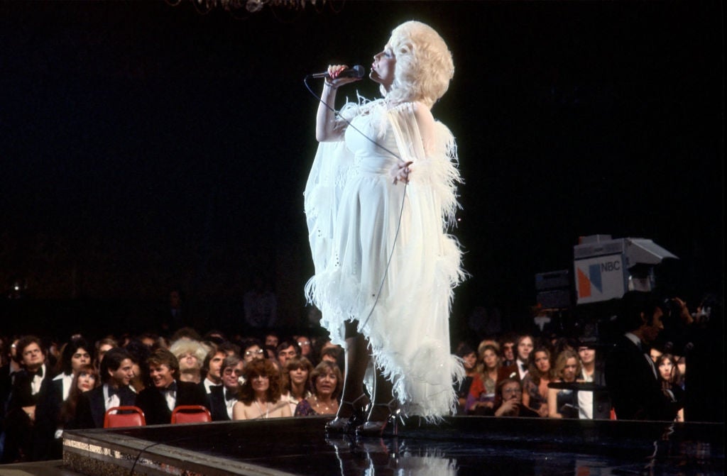 Singer in an elegant, feathered gown performs energetically on stage at a formal event, surrounded by an attentive audience