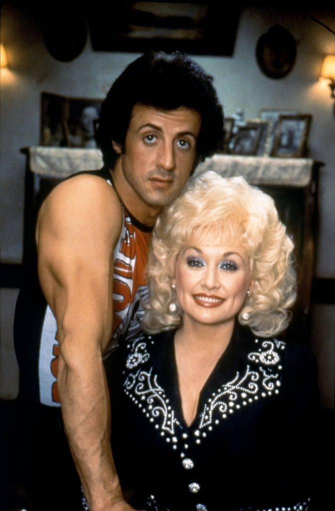 I don't know who the people in the image are, but they are posing together; the man is in a sleeveless top, and the woman is wearing a studded jacket