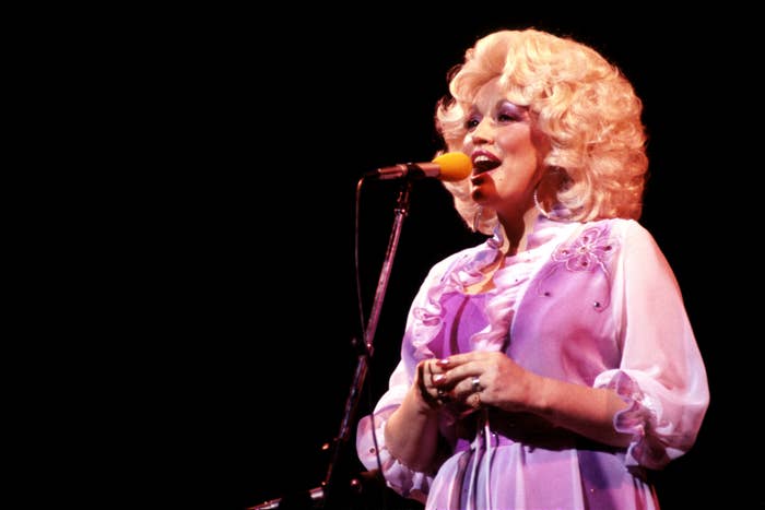 Singer in glamorous, vintage-style outfit with voluminous hair, performing on stage with a microphone