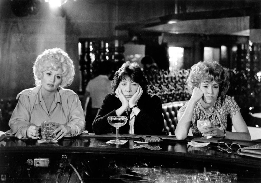 Three people sit at a bar, each with a drink, looking contemplative. Their attire features a mix of casual and patterned styles