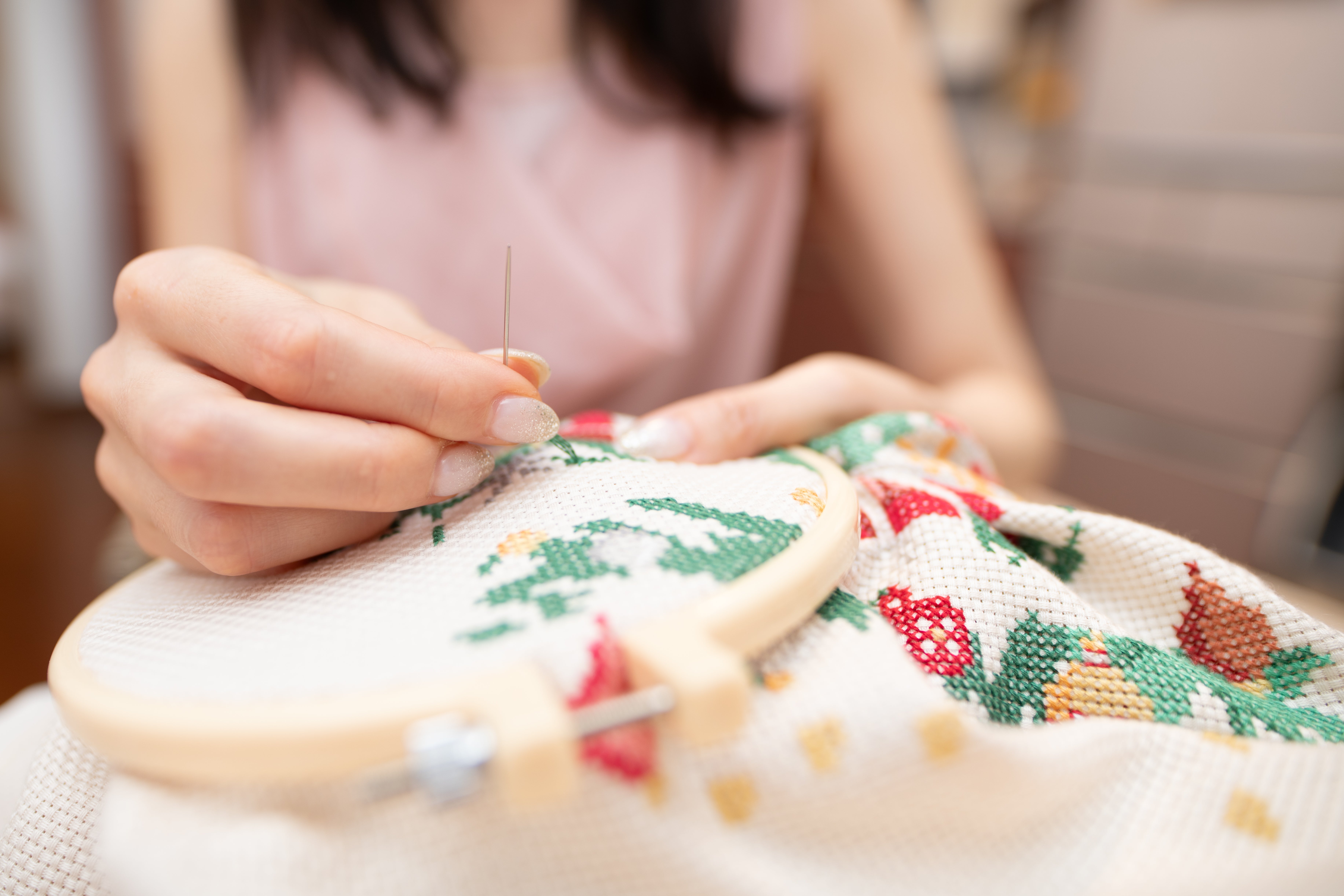 Person doing embroidery on fabric with colorful patterns, using a hoop to hold the cloth taut. Hands are carefully stitching the design