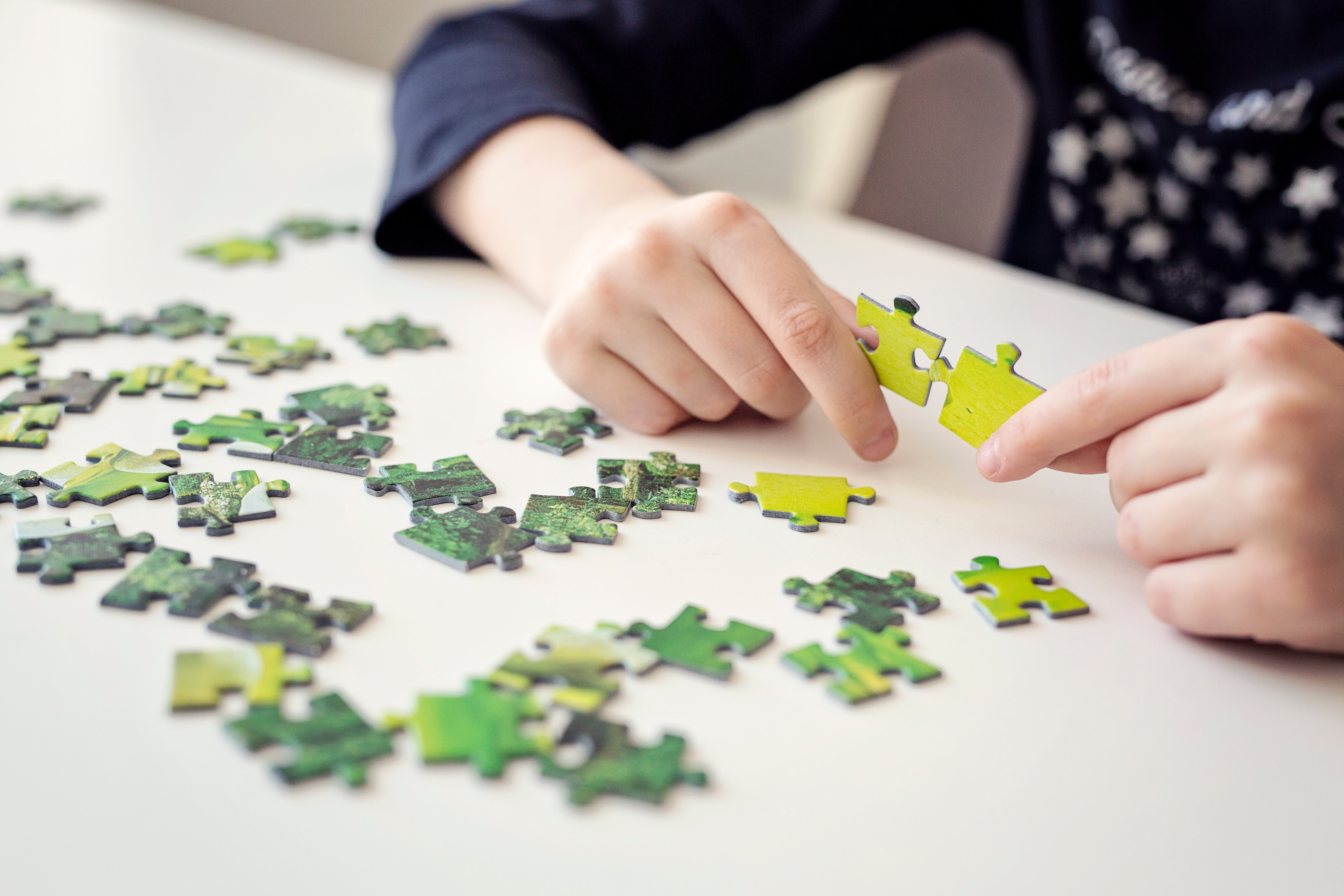 Person assembling a jigsaw puzzle on a table, demonstrating focus and fine motor skill activities beneficial for mental health