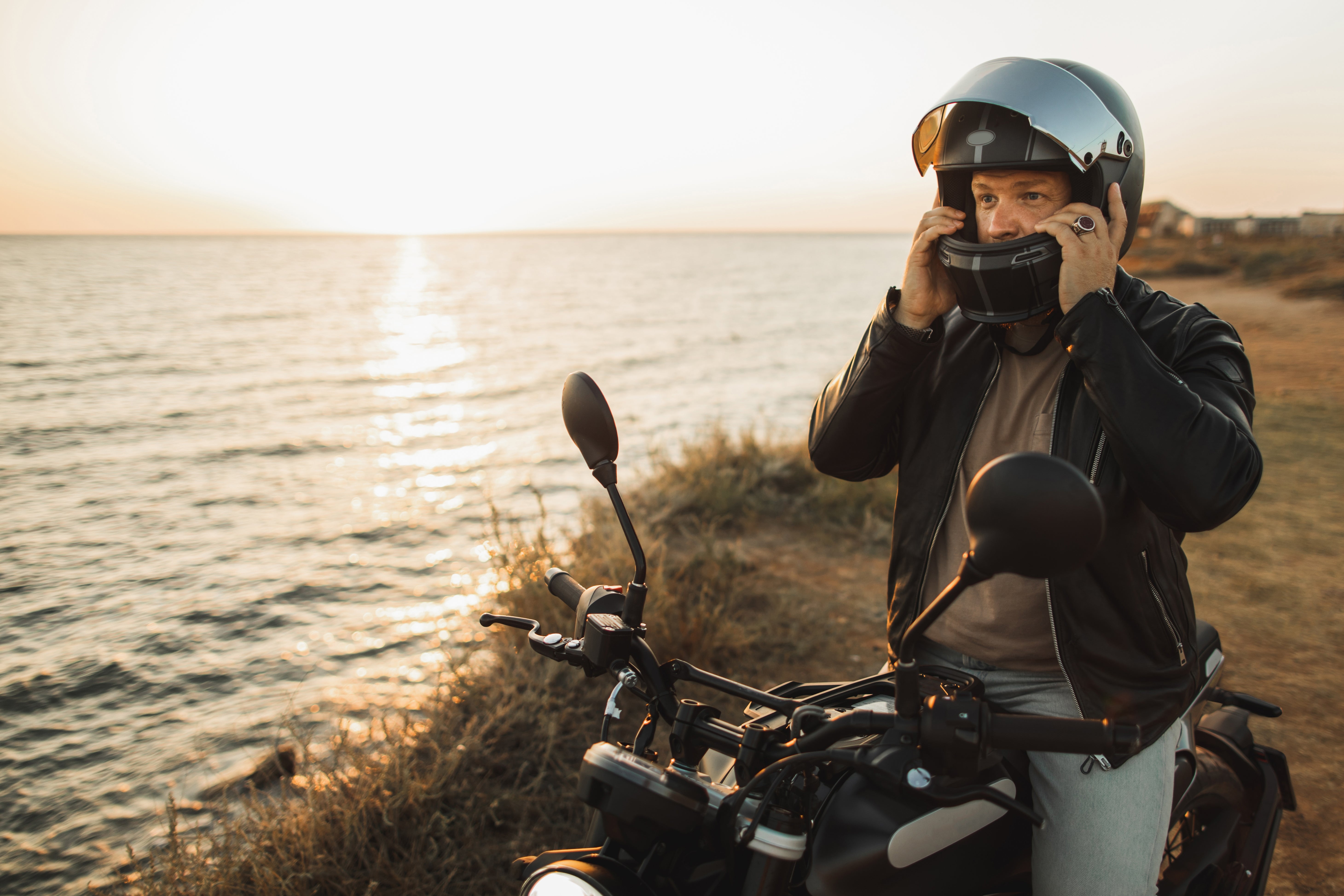 A person on a motorcycle near water wears a helmet, ensuring safety while enjoying a scenic view at sunset, highlighting outdoor wellness
