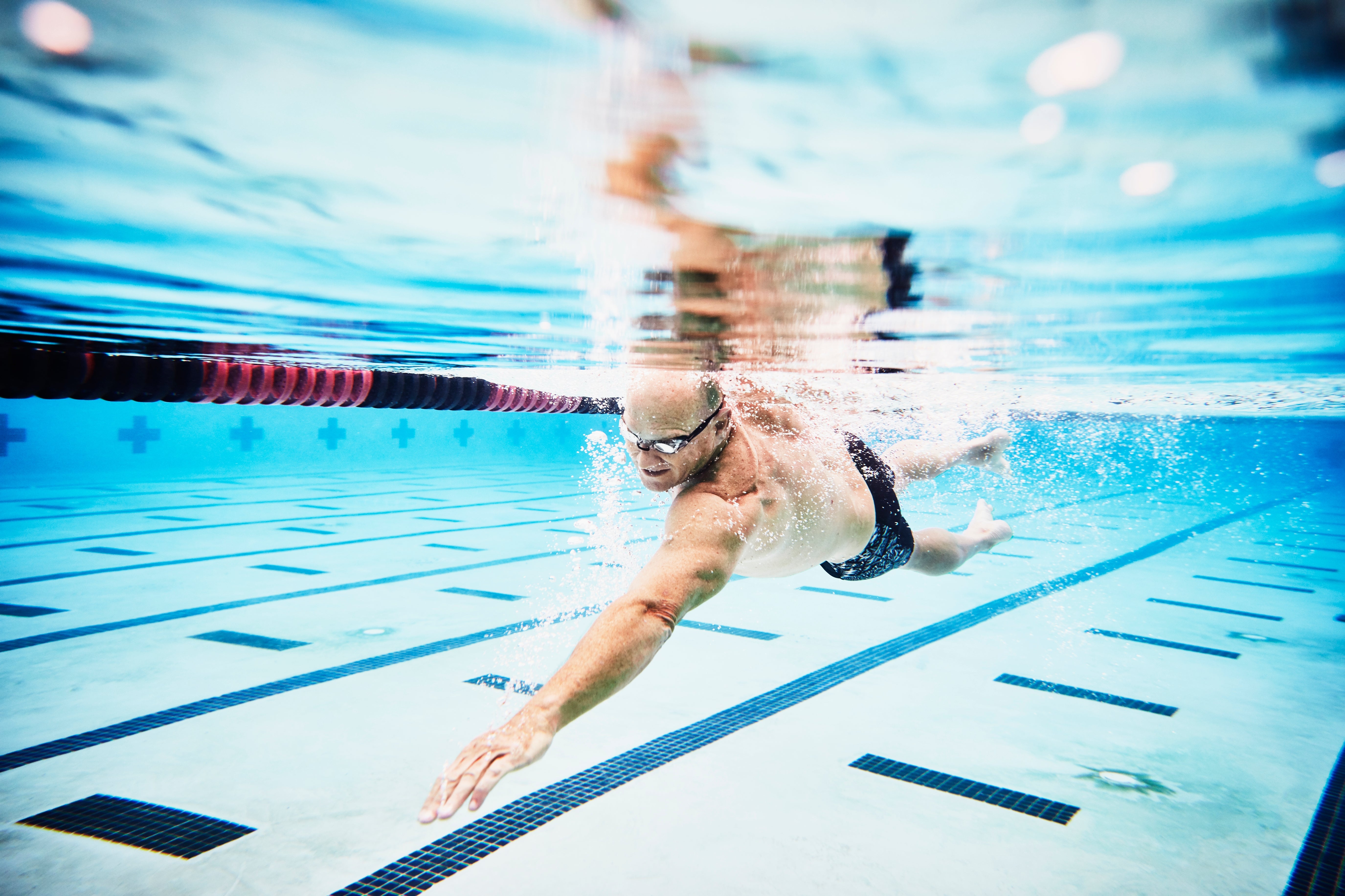A person swimming freestyle in a pool, wearing goggles, emphasizing an active and healthy lifestyle