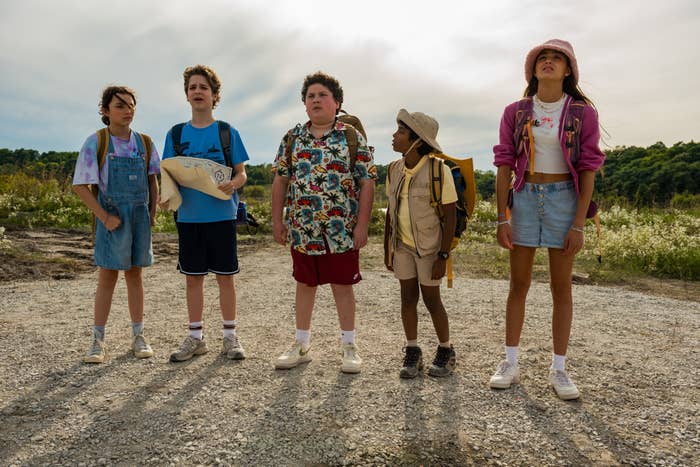 Five young people standing outside; they wear casual, adventure-themed outfits