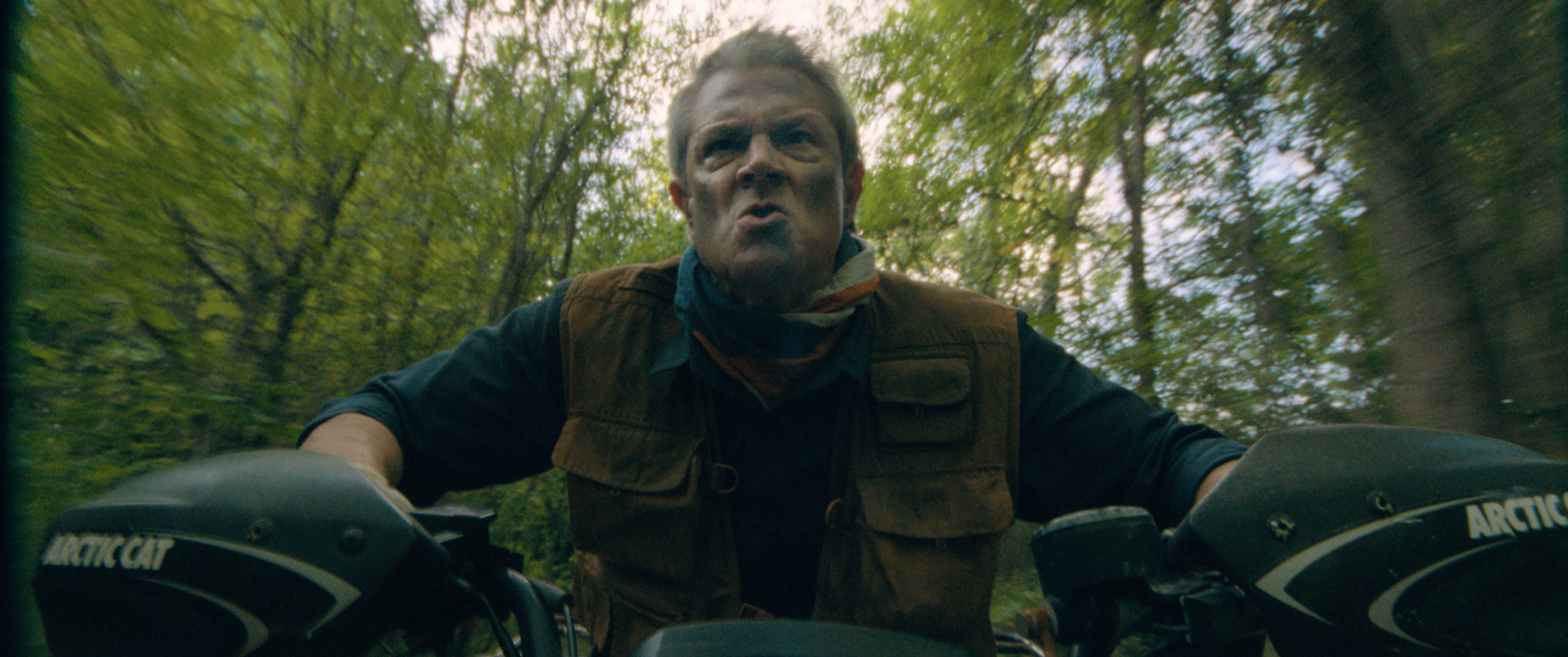 Person riding an Arctic Cat ATV through a forest, looking determined