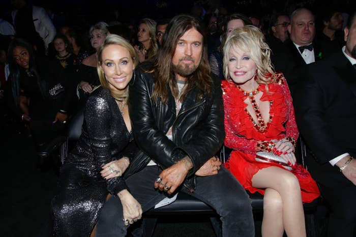 Three people sit together at an event. The person on the right wears a red dress with ruffles