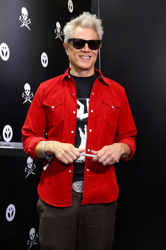 Person in a red button-up shirt over a graphic tee, wearing sunglasses, smiles at a public event