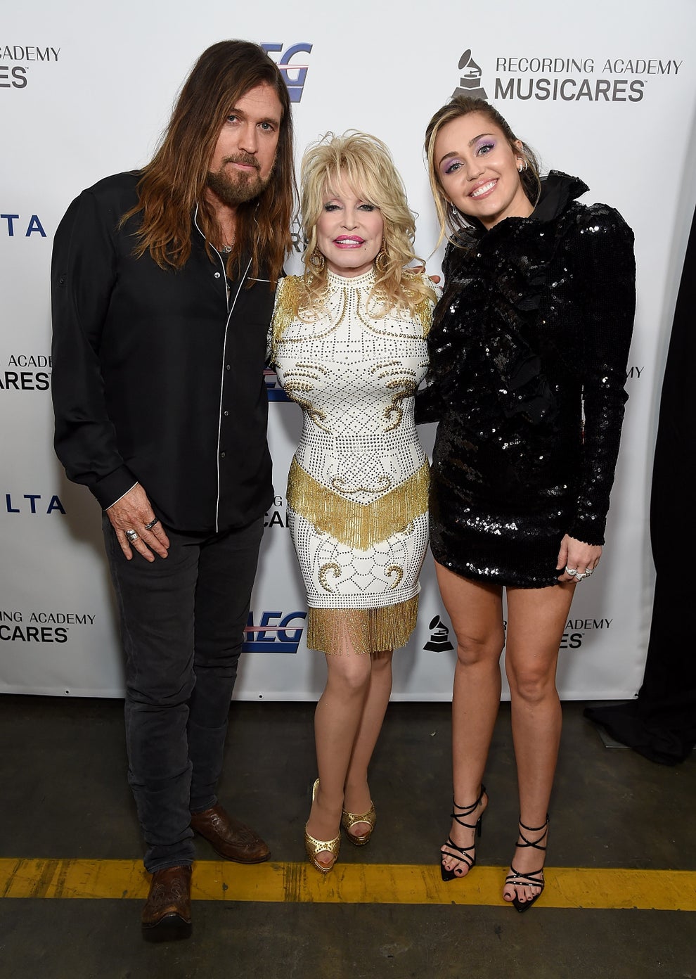 Three people posing at a celebrity event, dressed in stylish evening attire