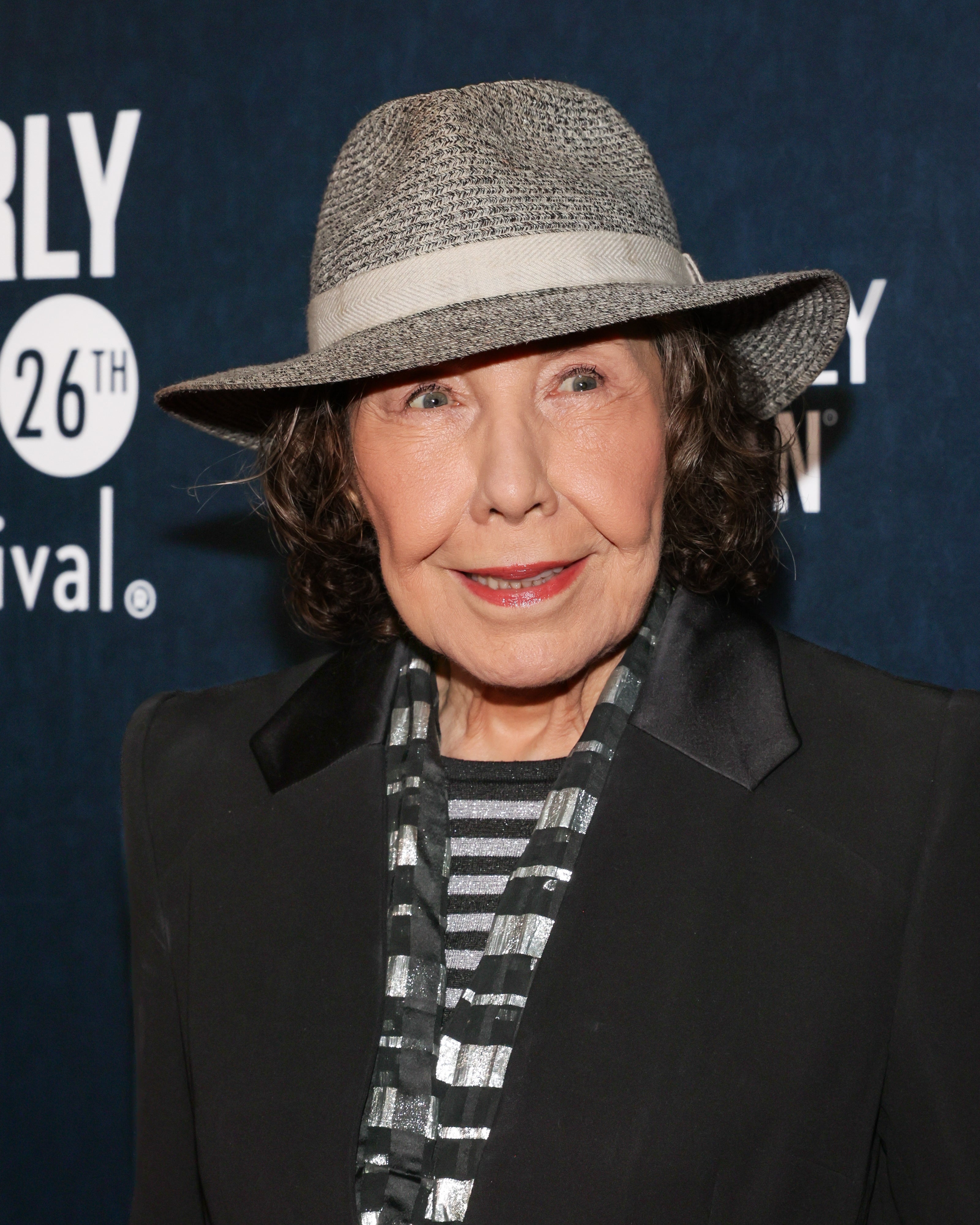 Person wearing a suit and striped shirt, accessorized with a patterned scarf and hat, attending a formal event