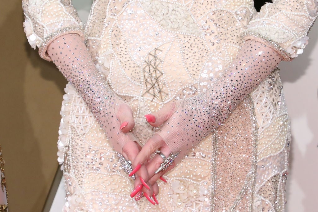 Close-up of person in an intricately beaded outfit with embellished gloves, hands crossed. Focus on detailed texture and sparkling embellishments