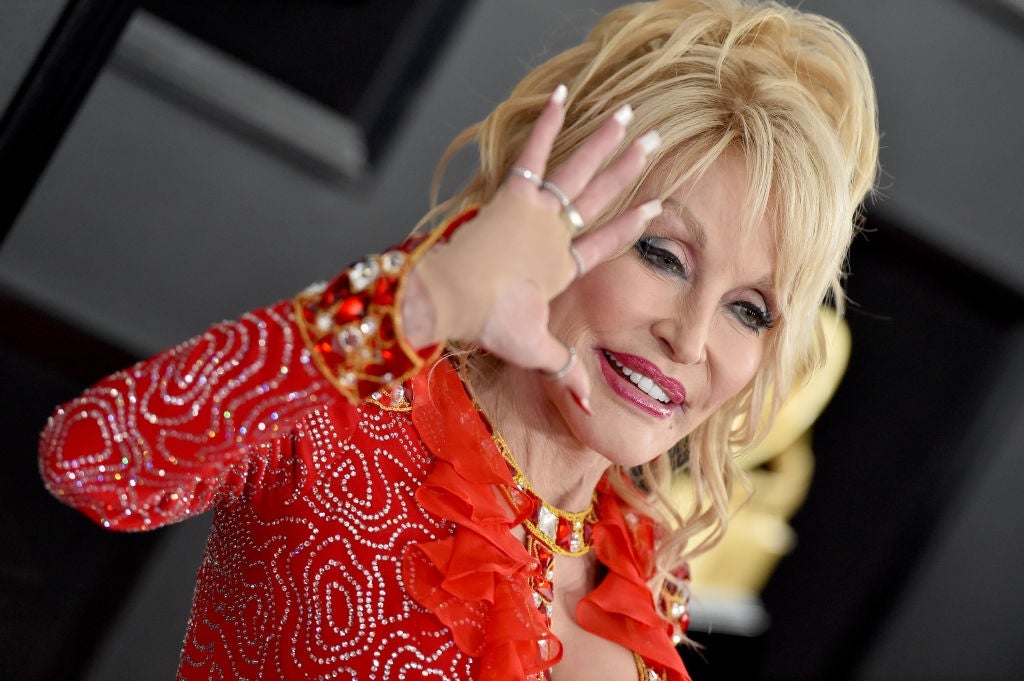 Person in sequined dress waves with a smile