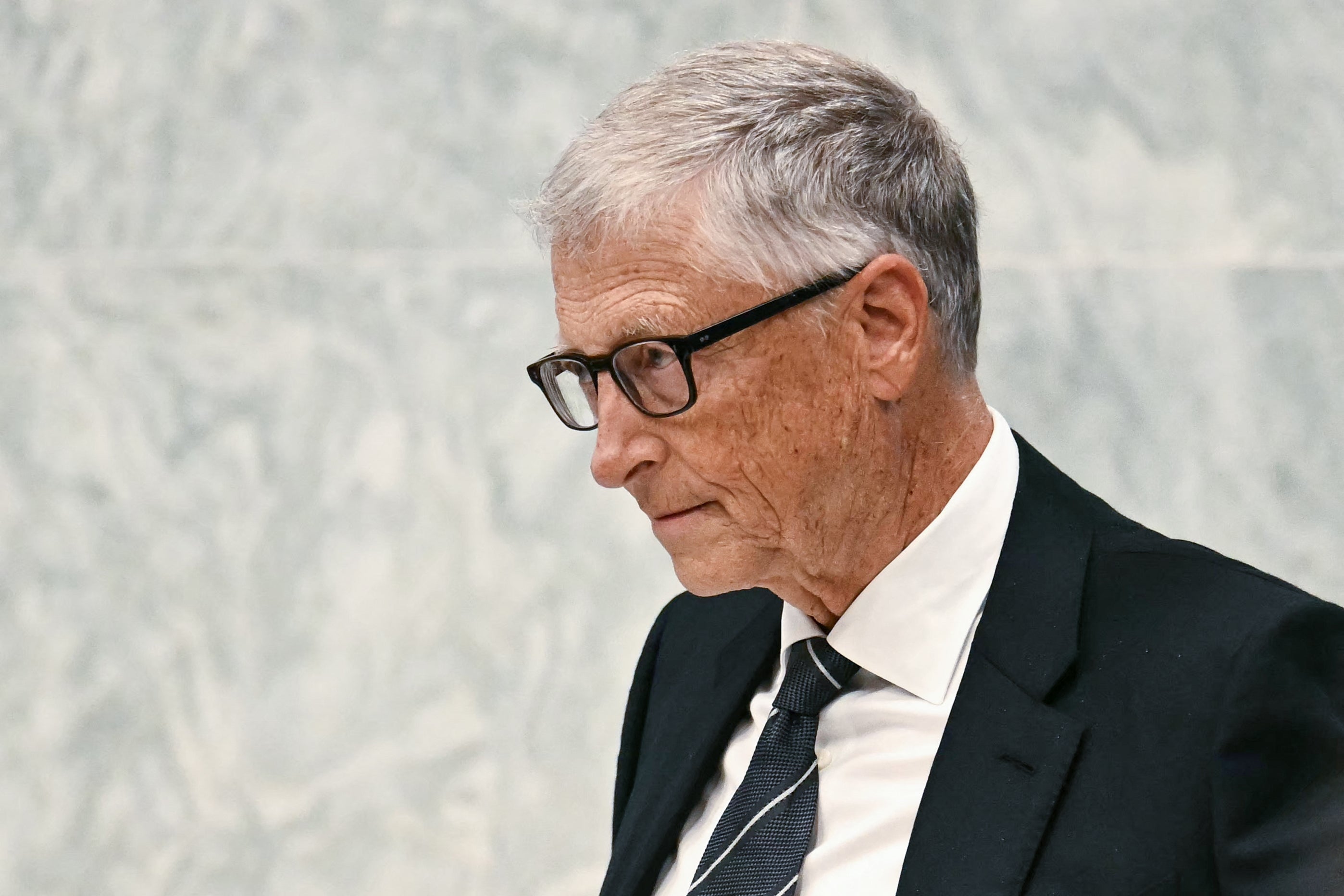 Elderly man in a suit with glasses looks thoughtful, attending a formal event