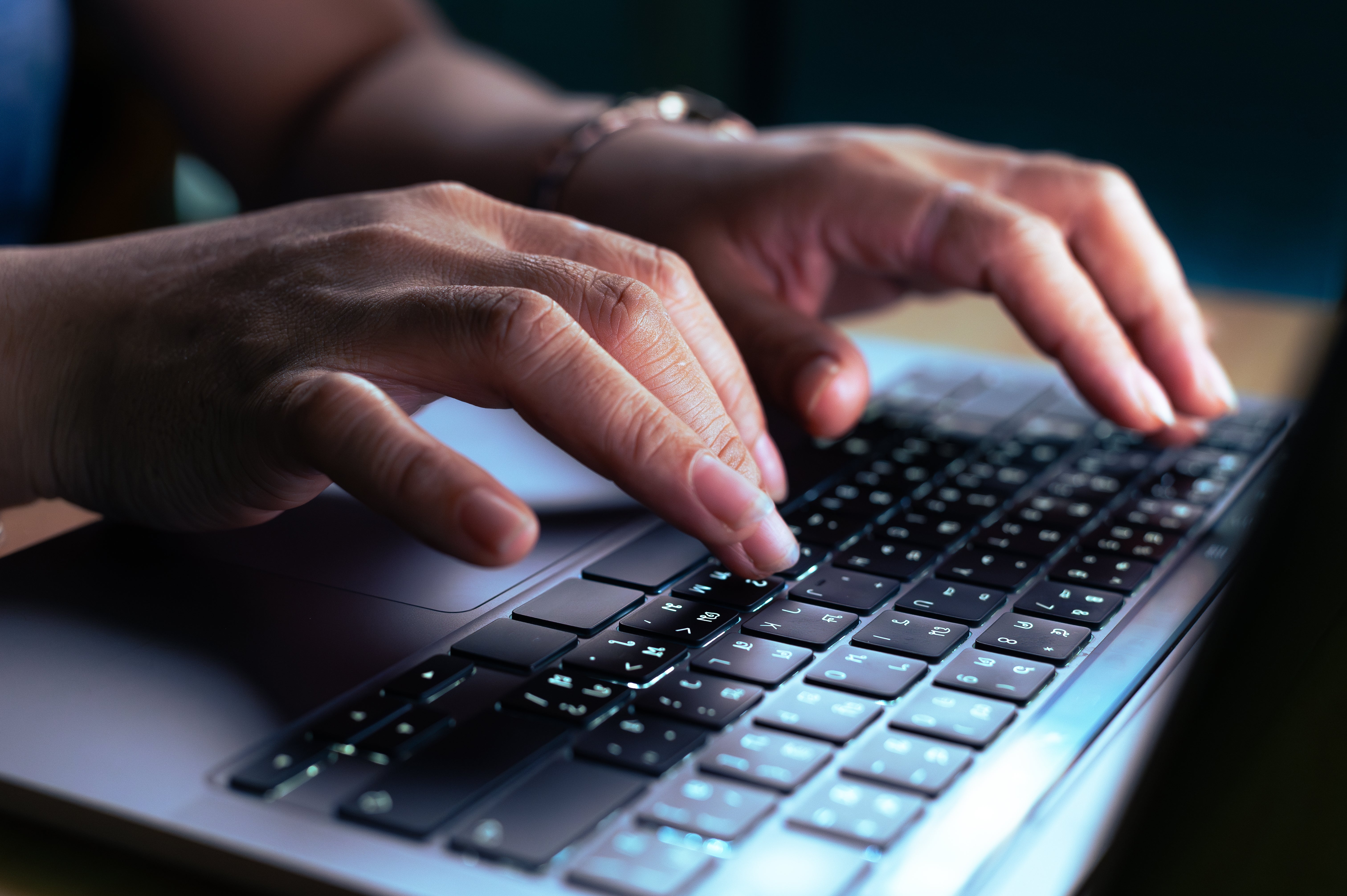 Hands typing on a laptop keyboard, suggesting focused work or online activity