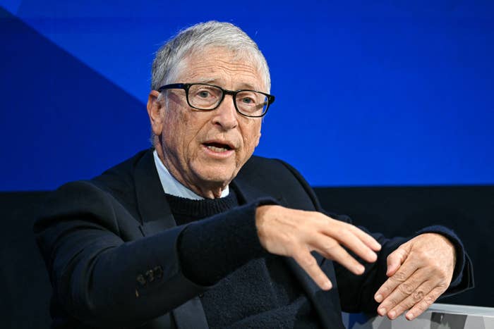 A person in a suit, seated, gesturing while speaking at an event