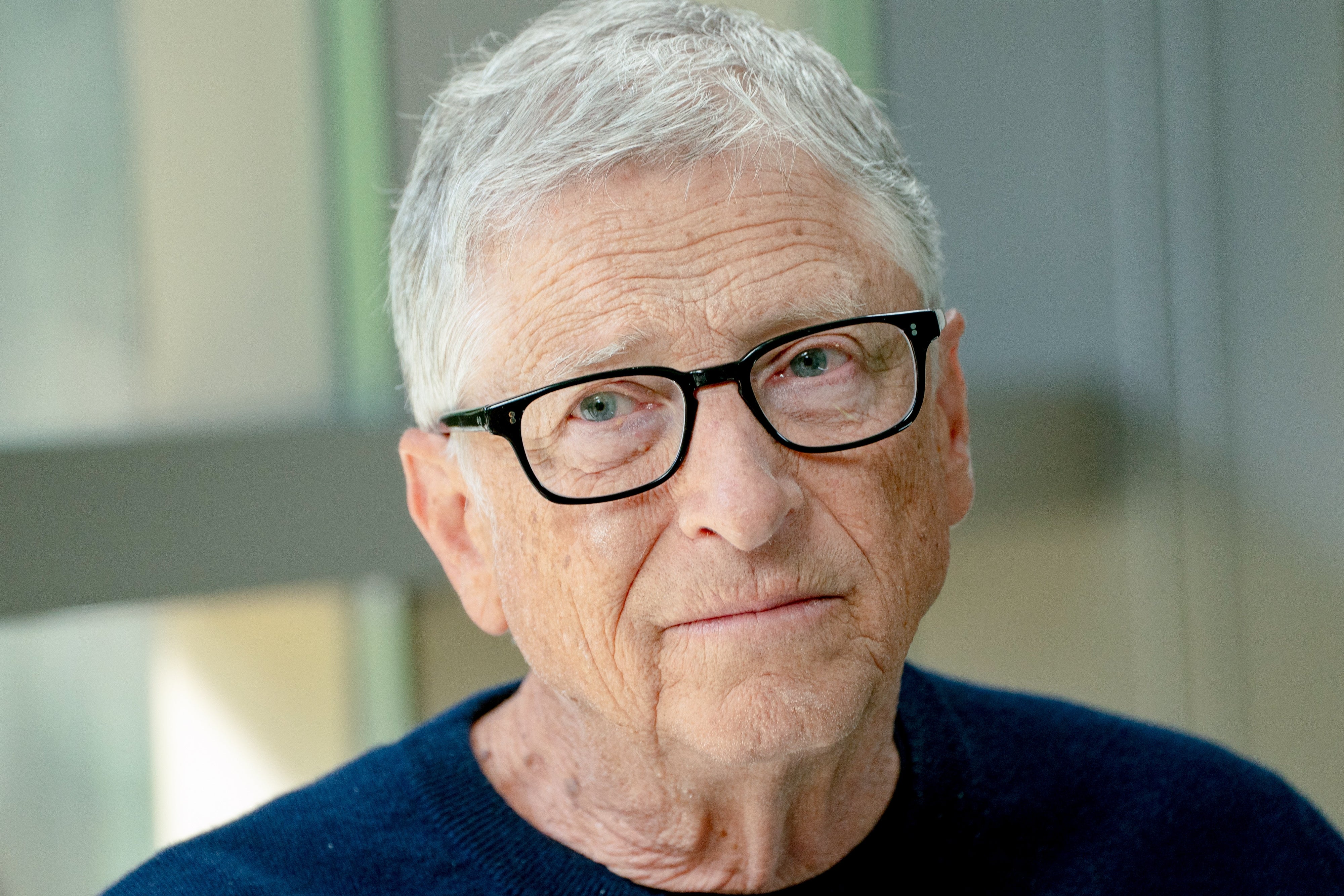 A person with short hair and glasses is looking toward the camera, wearing a simple, casual sweater