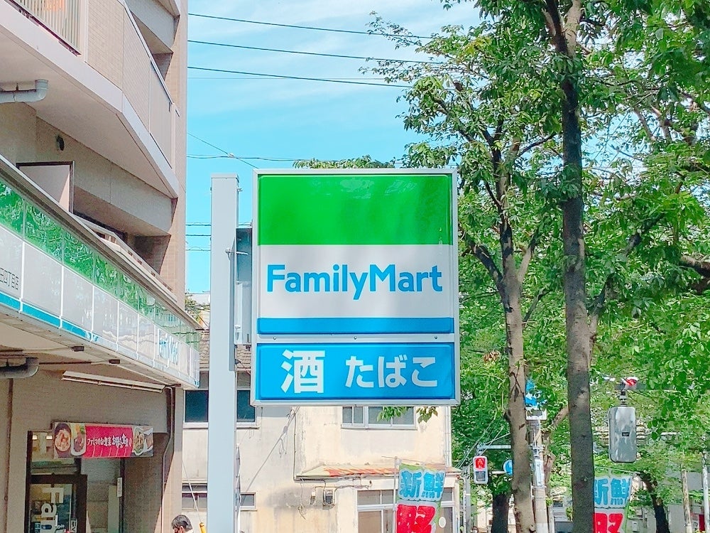 ファミリーマートの看板。周囲に木々と他の建物が見える街の一角。