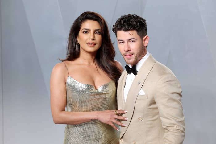 Two celebrities pose together; the woman wears a shimmery gown, and the man wears a tan suit with a bow tie