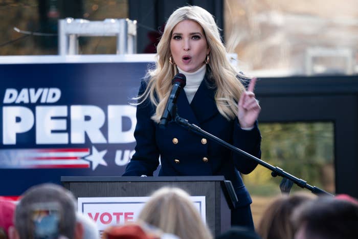 Person speaking at a podium during an outdoor event with a political campaign sign in the background