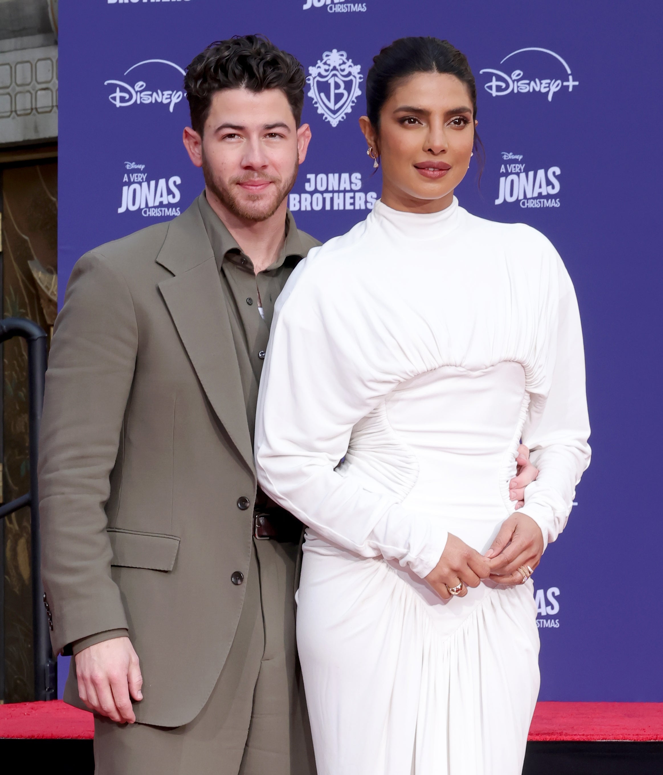 A woman in a chic long-sleeved gown poses with a man in a smart suit at a red carpet event