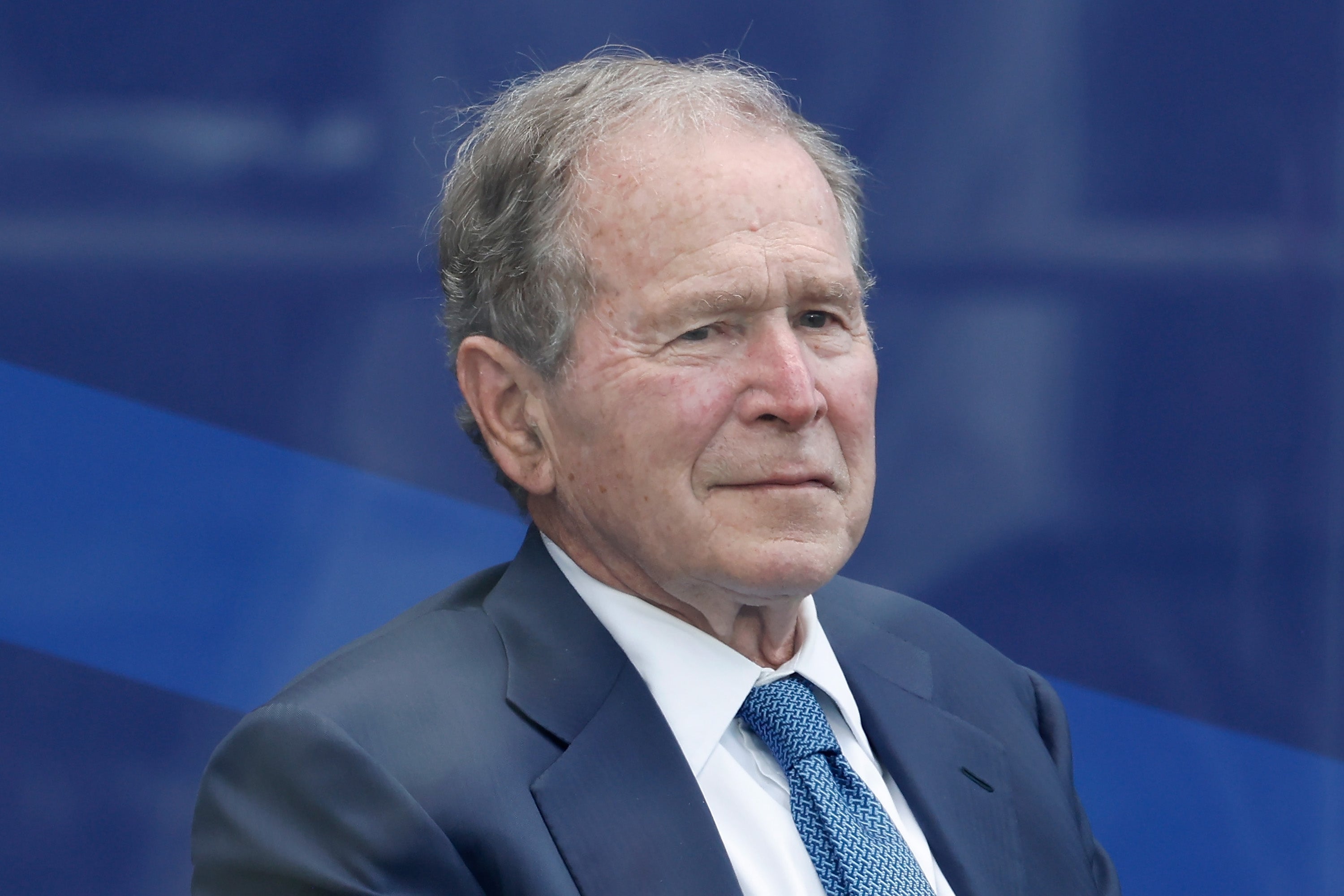 An older man in a suit and tie is seated, gazing forward with a calm expression