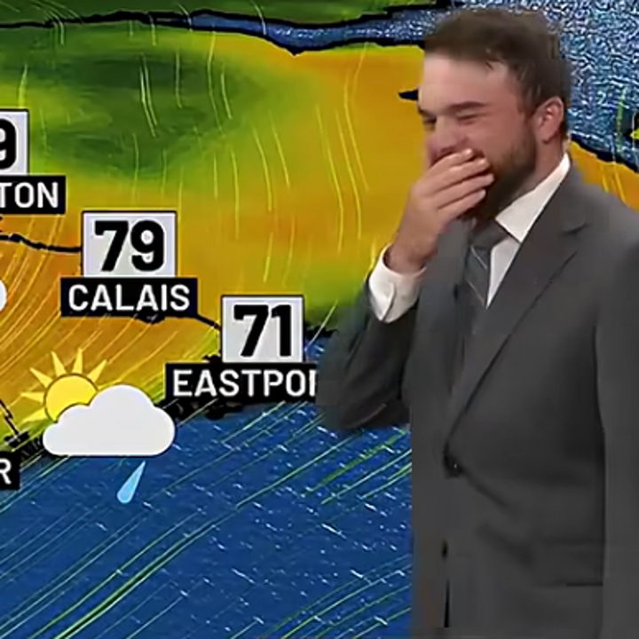 Meteorologist in a suit smiles and covers mouth on live weather forecast. Temperatures and rain are shown for various cities
