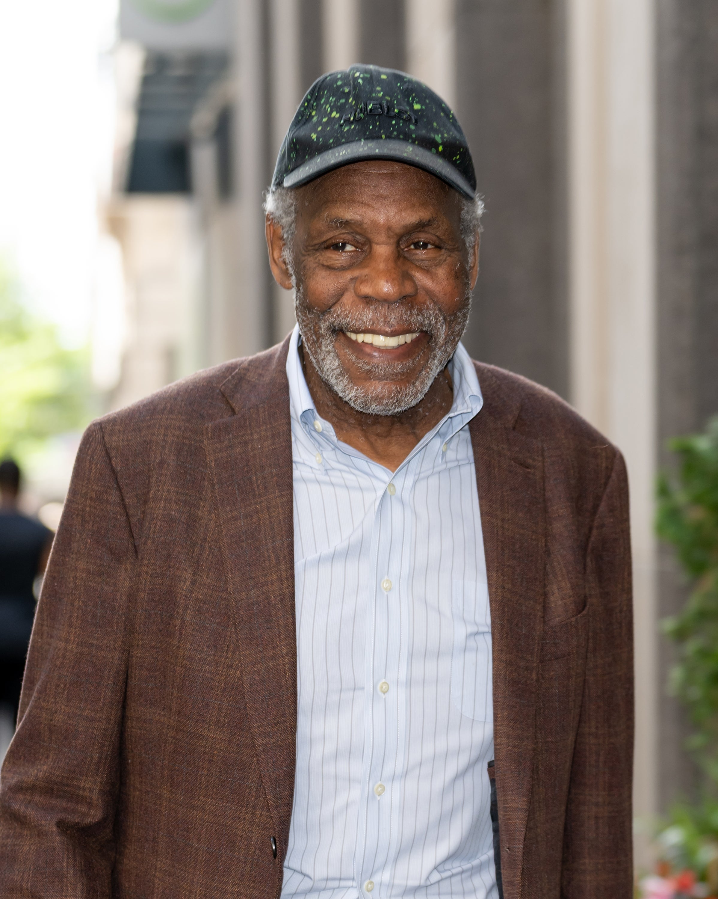 A smiling man in a striped shirt, blazer, and cap, standing outdoors