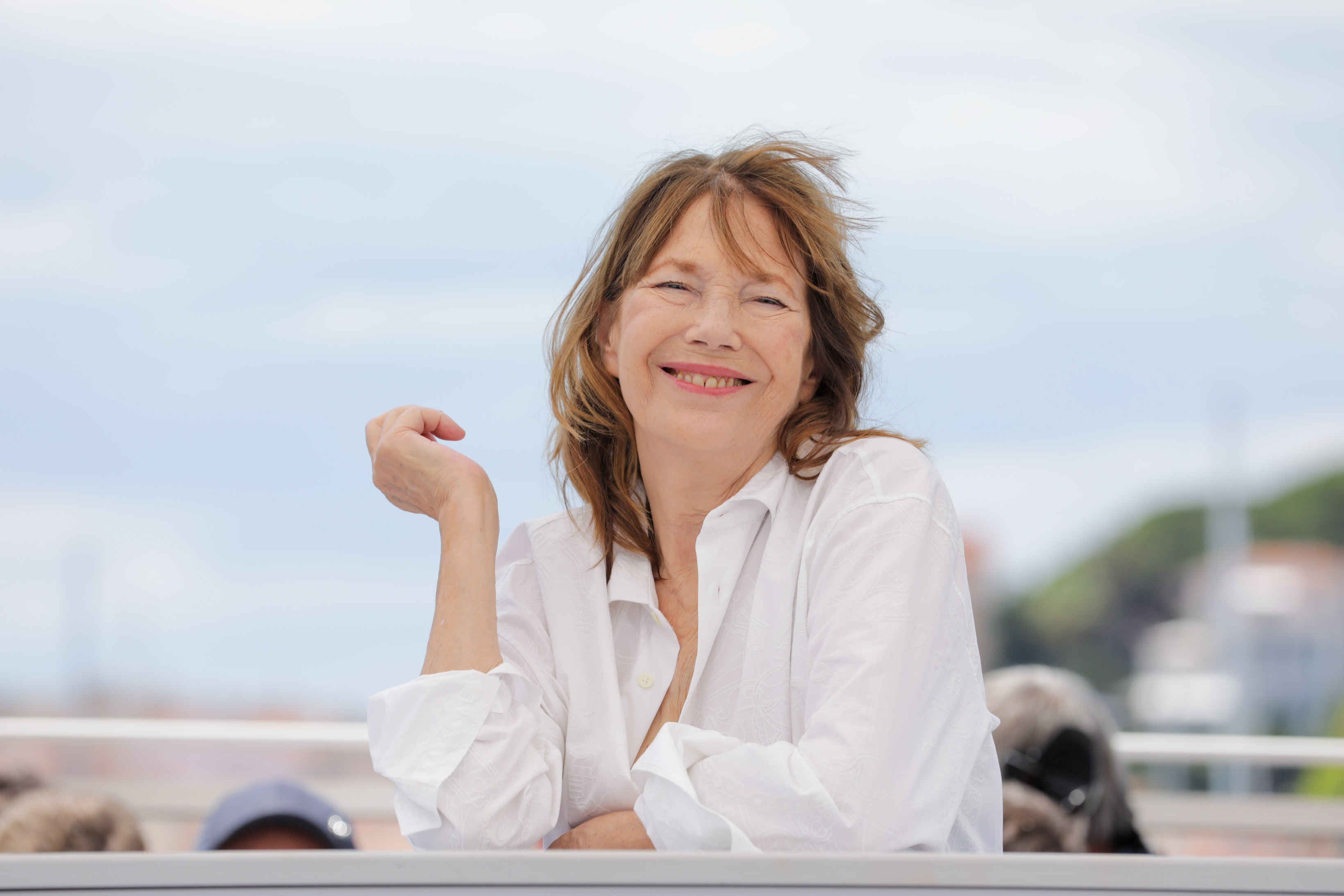 Person smiling, wearing a casual button-up shirt, outdoors with a blurred background
