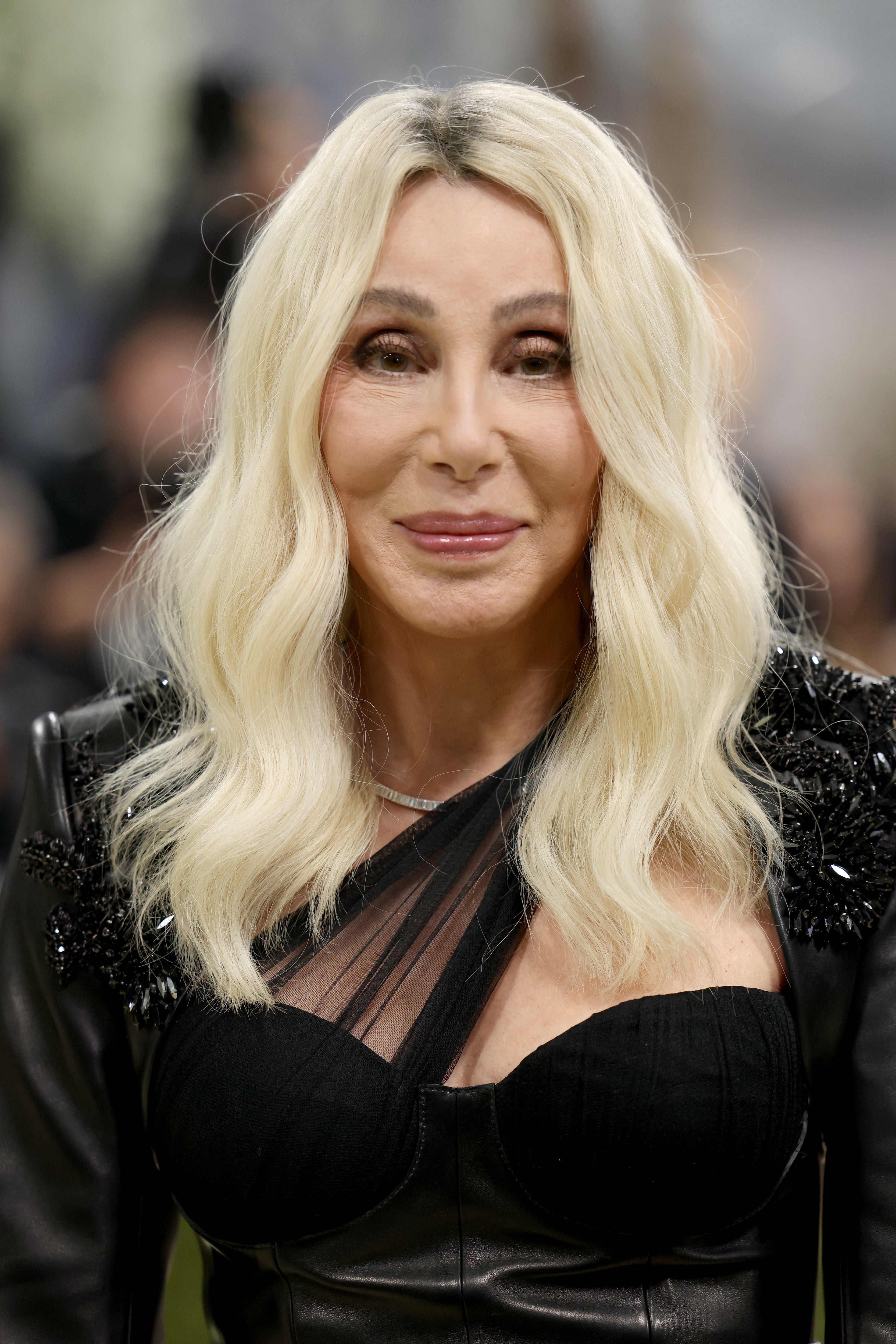Person on the red carpet wears a stylish black dress with sheer panels and embellished shoulders. They have long, wavy hair