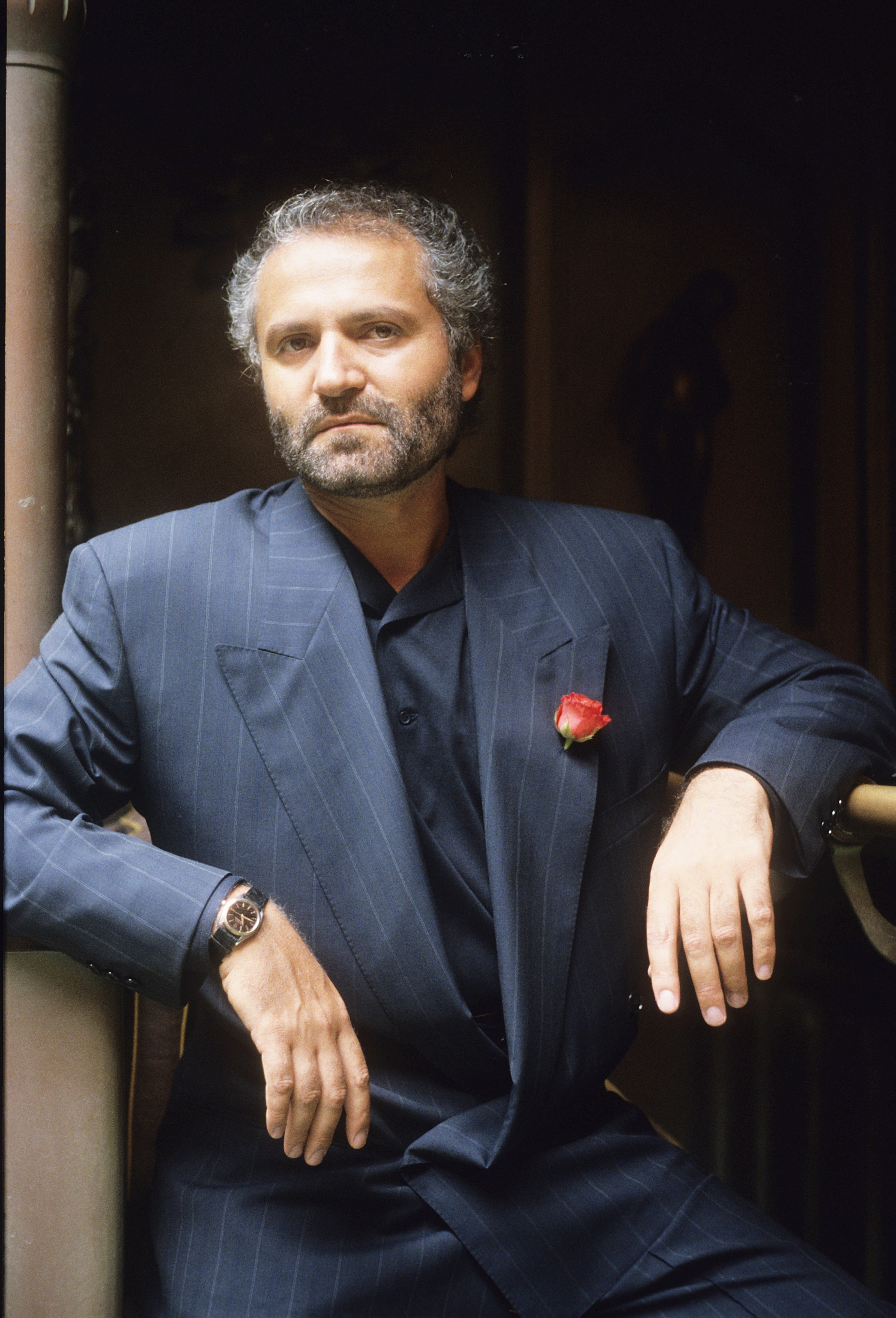 Man in a dark pinstripe suit with a rose pin, leaning on a railing