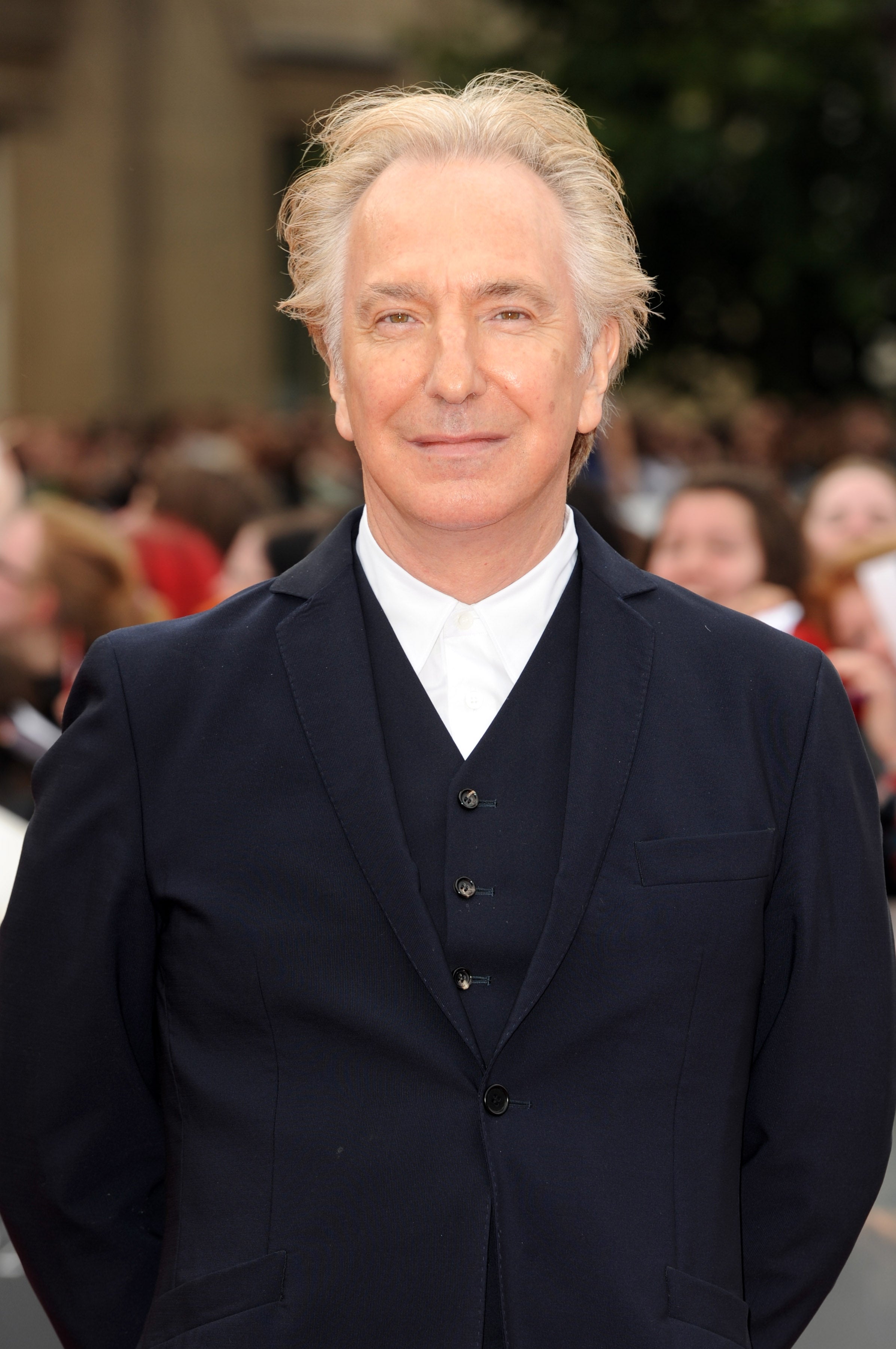 Person in a formal three-piece suit standing on a red carpet, smiling at the camera