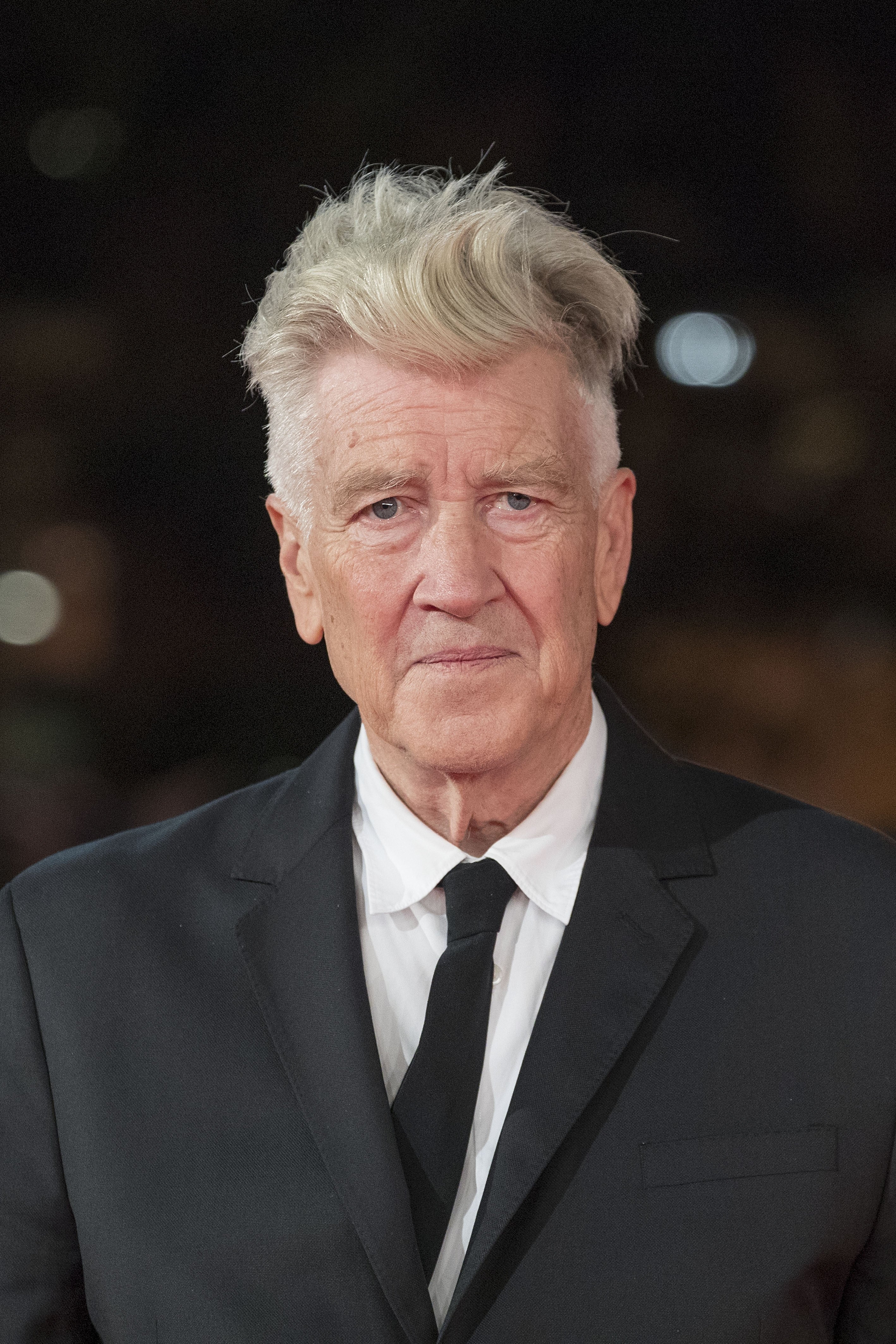 I don't know who this person is. An older gentleman is wearing a classic suit and tie at a formal event, looking directly at the camera