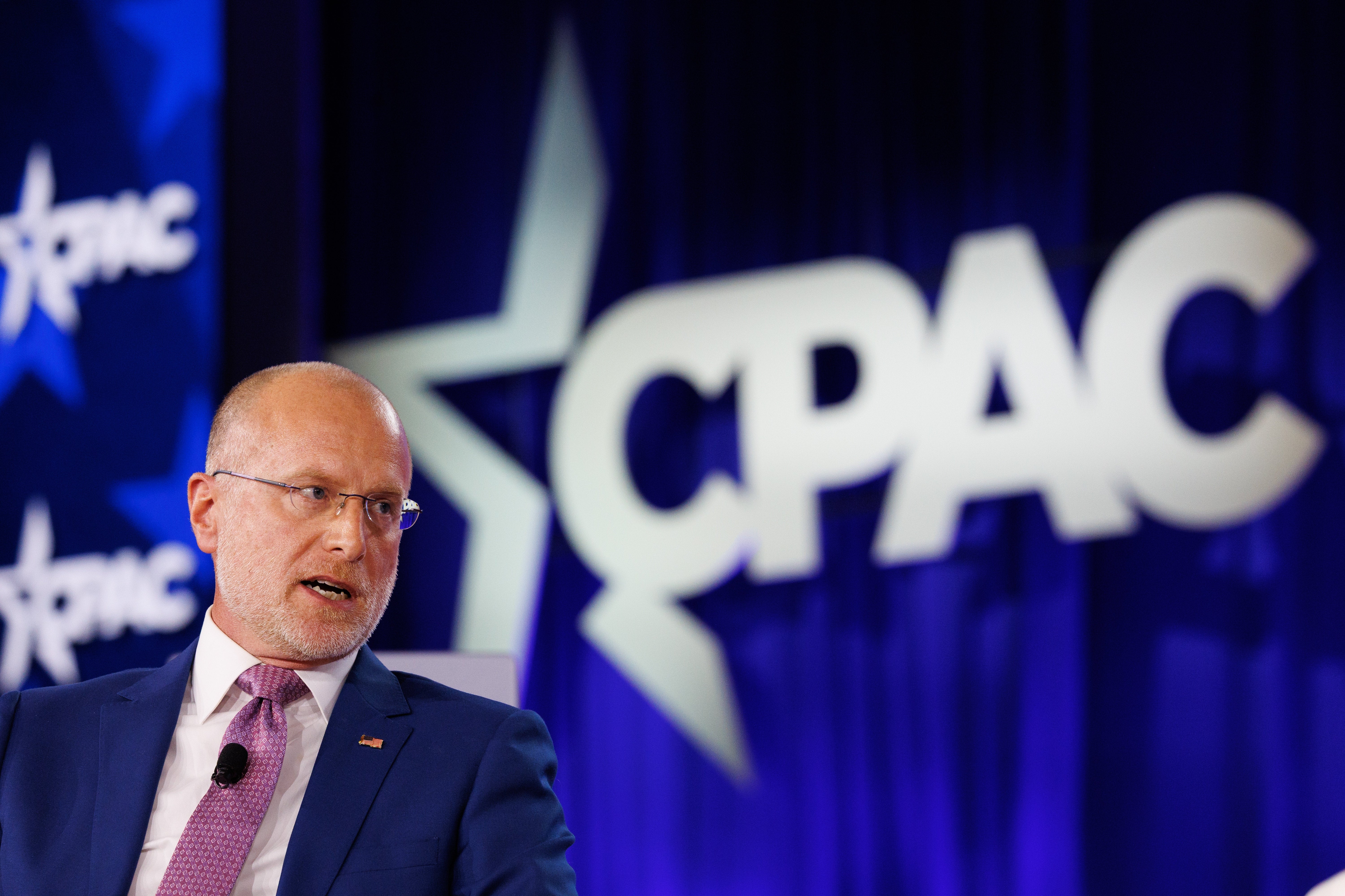 En person i dress taler ved et podium på CPAC. Bakteppet har en CPAC-logo med en stor stjernedesign