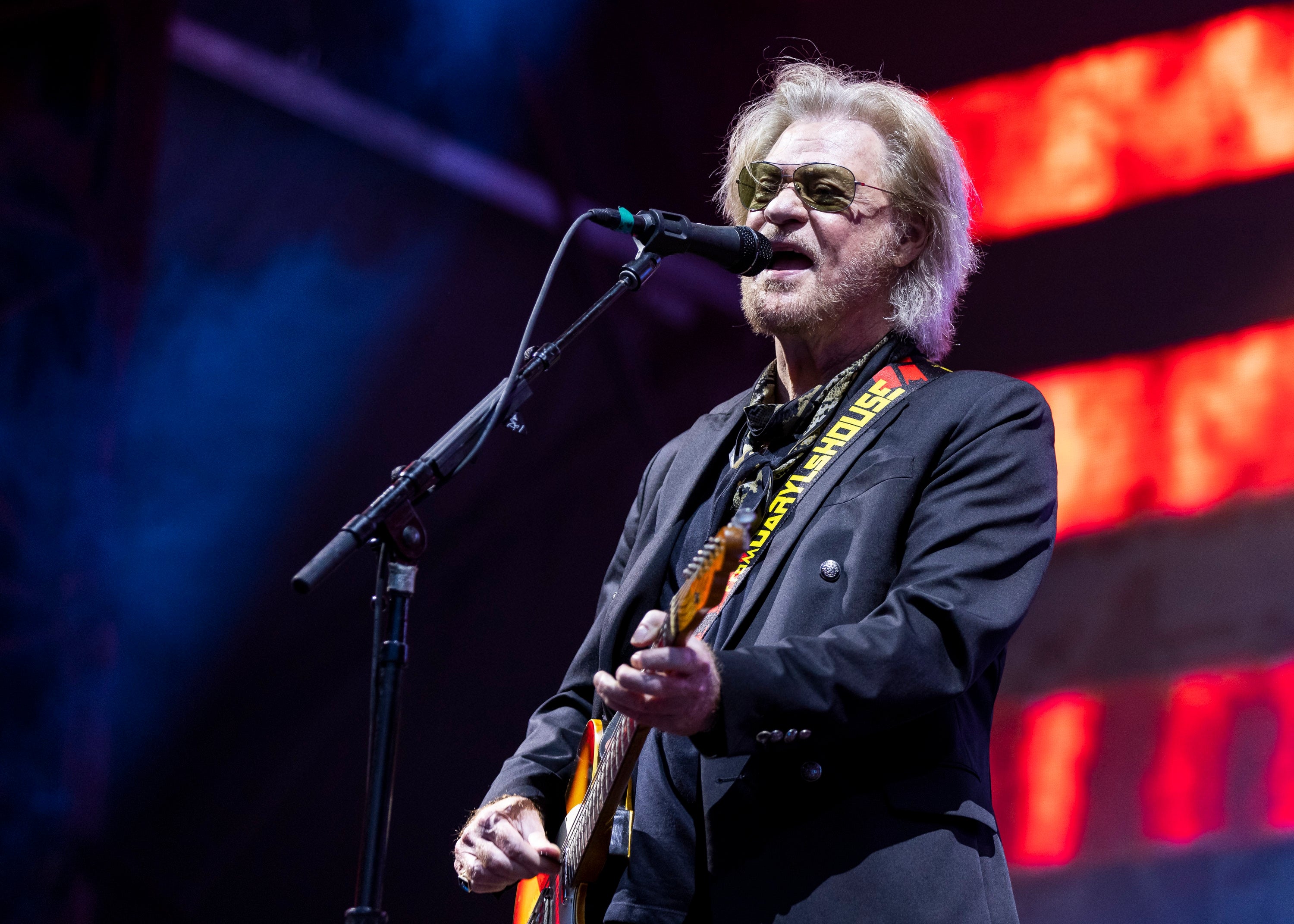 Musician performing on stage with a guitar, wearing a dark suit and sunglasses