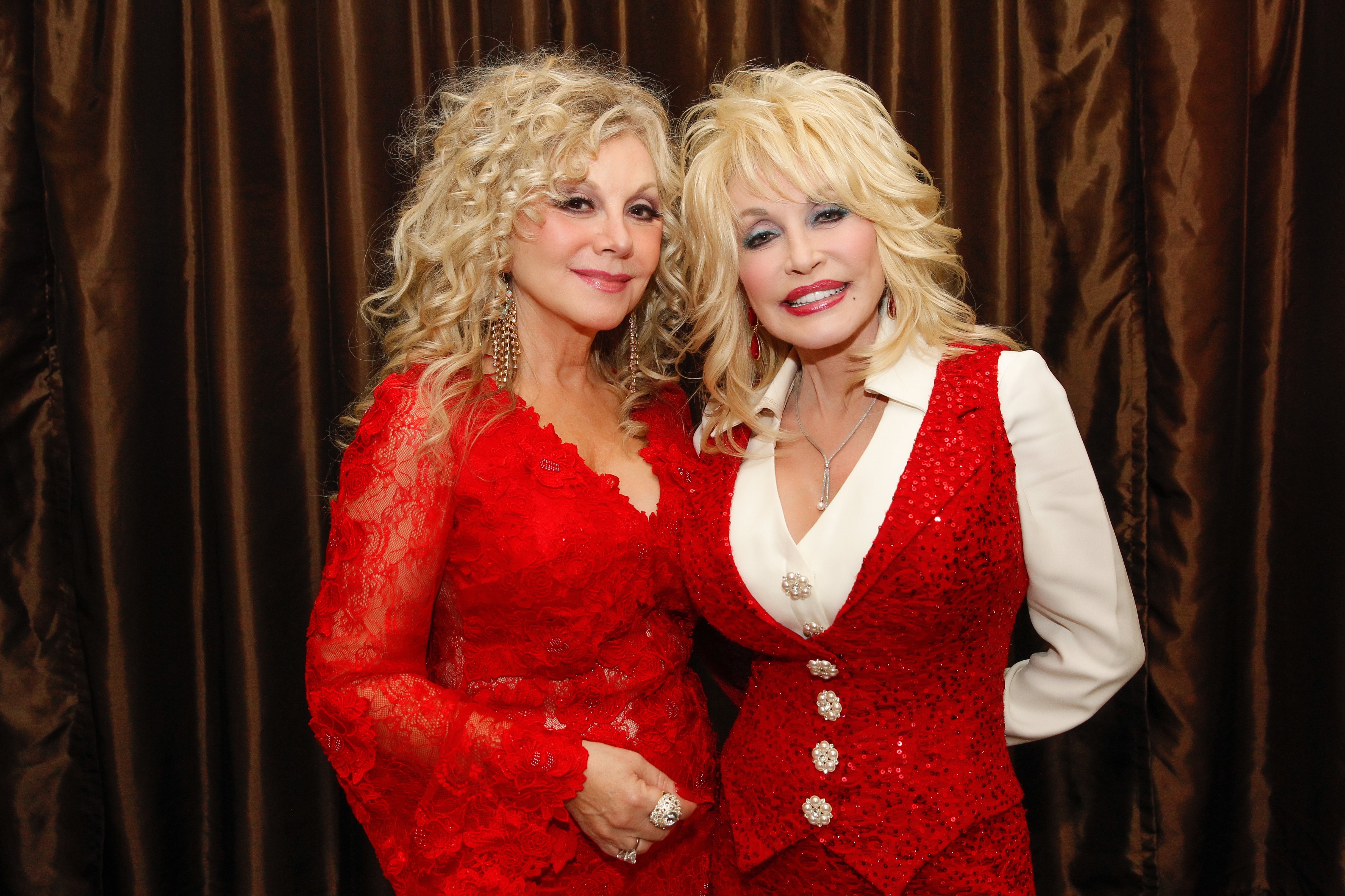 Two celebrities wearing elegant red lace outfits, posing together at an event, smiling for the camera