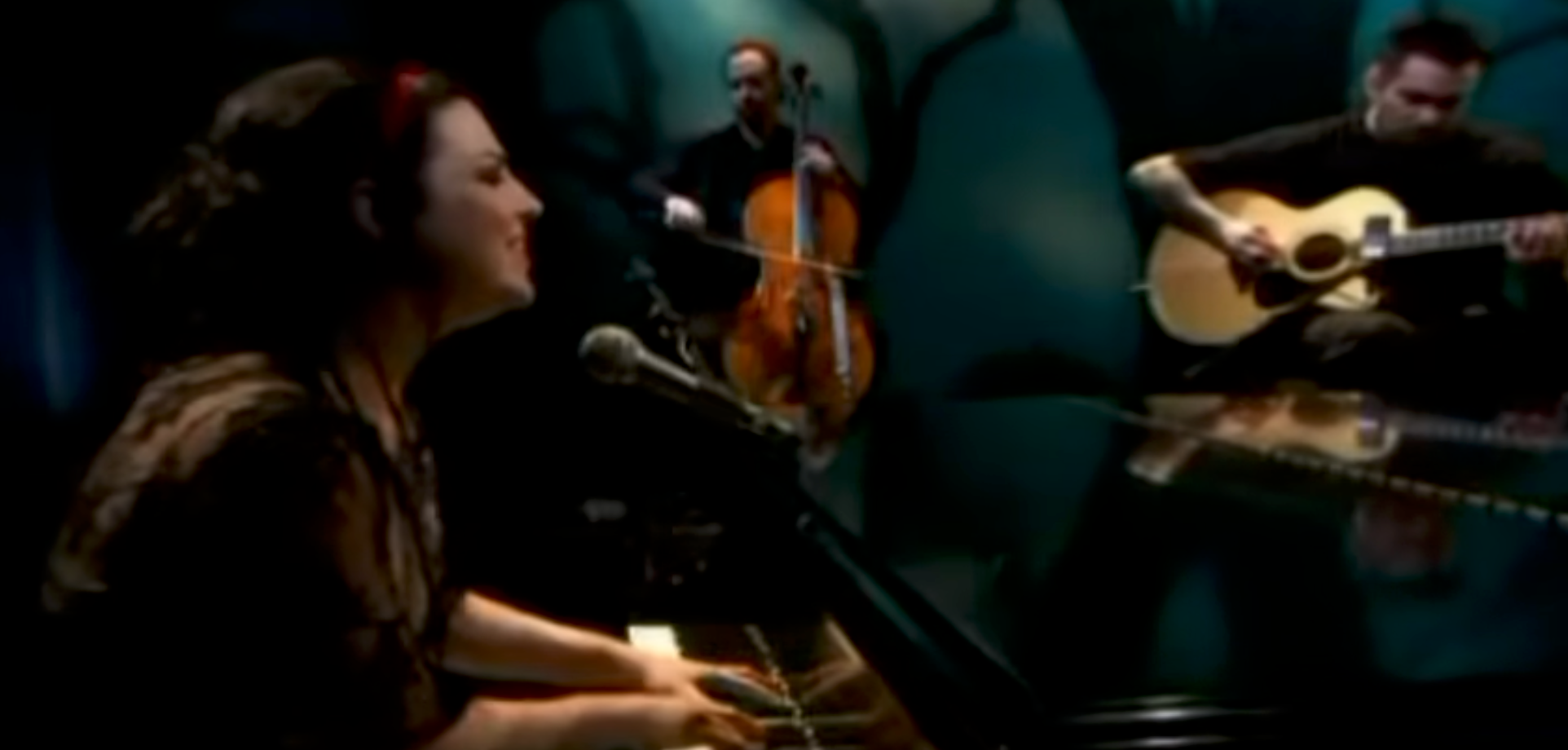 Musicians perform on stage with piano, cello, and guitar, creating an intimate musical atmosphere