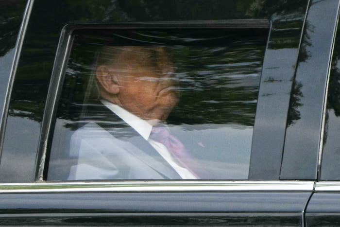 A person in formal attire appears pensive, seated in the back of a car, partially obscured by window reflections