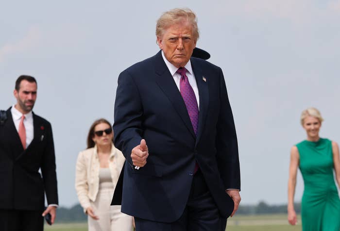 Person in a suit with a pink tie walks confidently outdoors, followed by formally dressed individuals