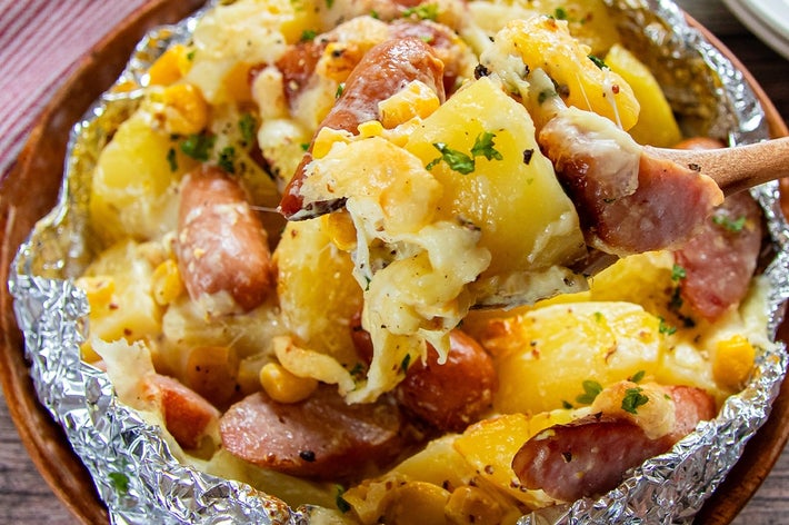 フォークにすくわれたホイルに包まれたソーセージとじゃがいもの料理。