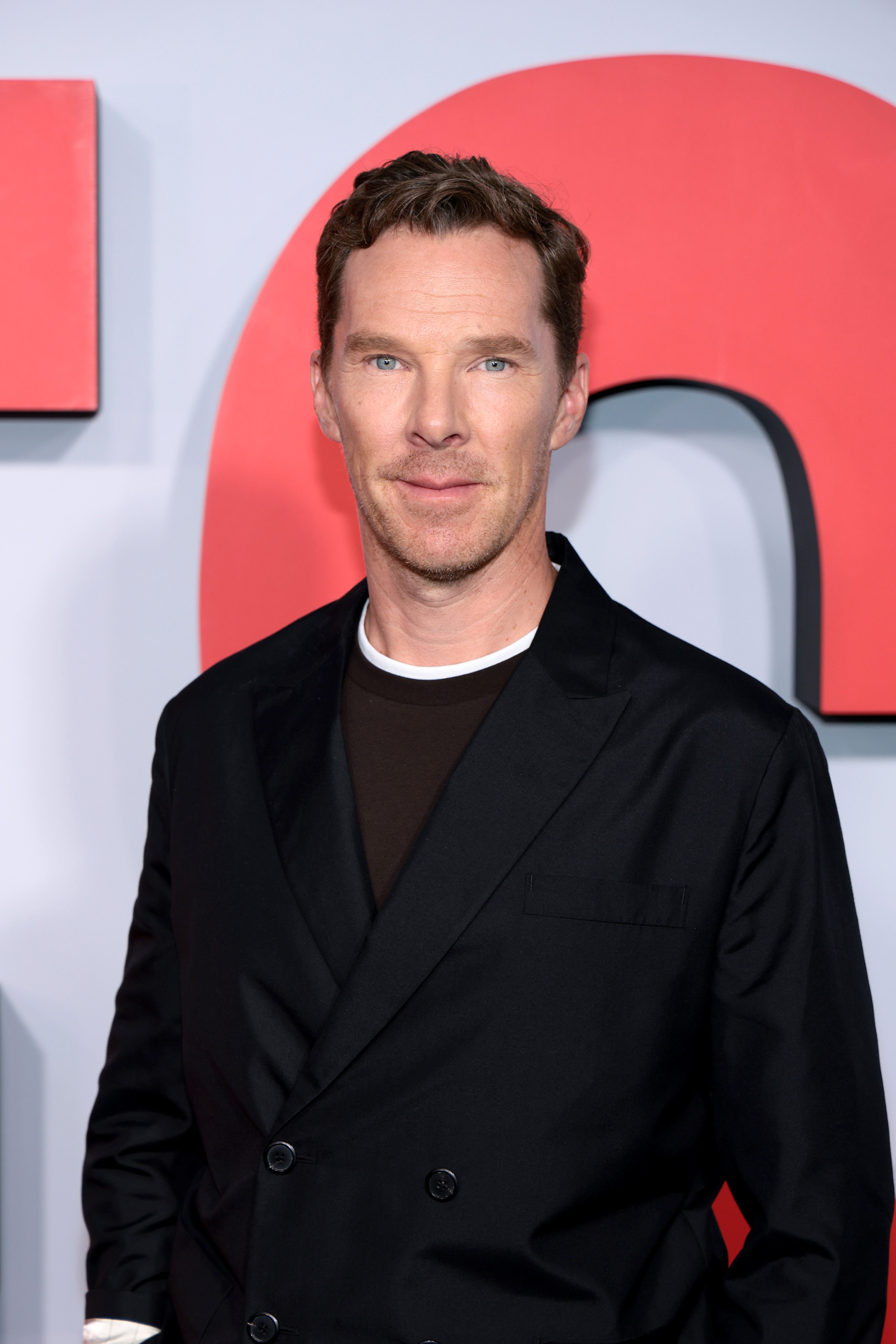 Benedict Cumberbatch on the red carpet wearing a stylish black suit over a dark crewneck shirt, posing for photos