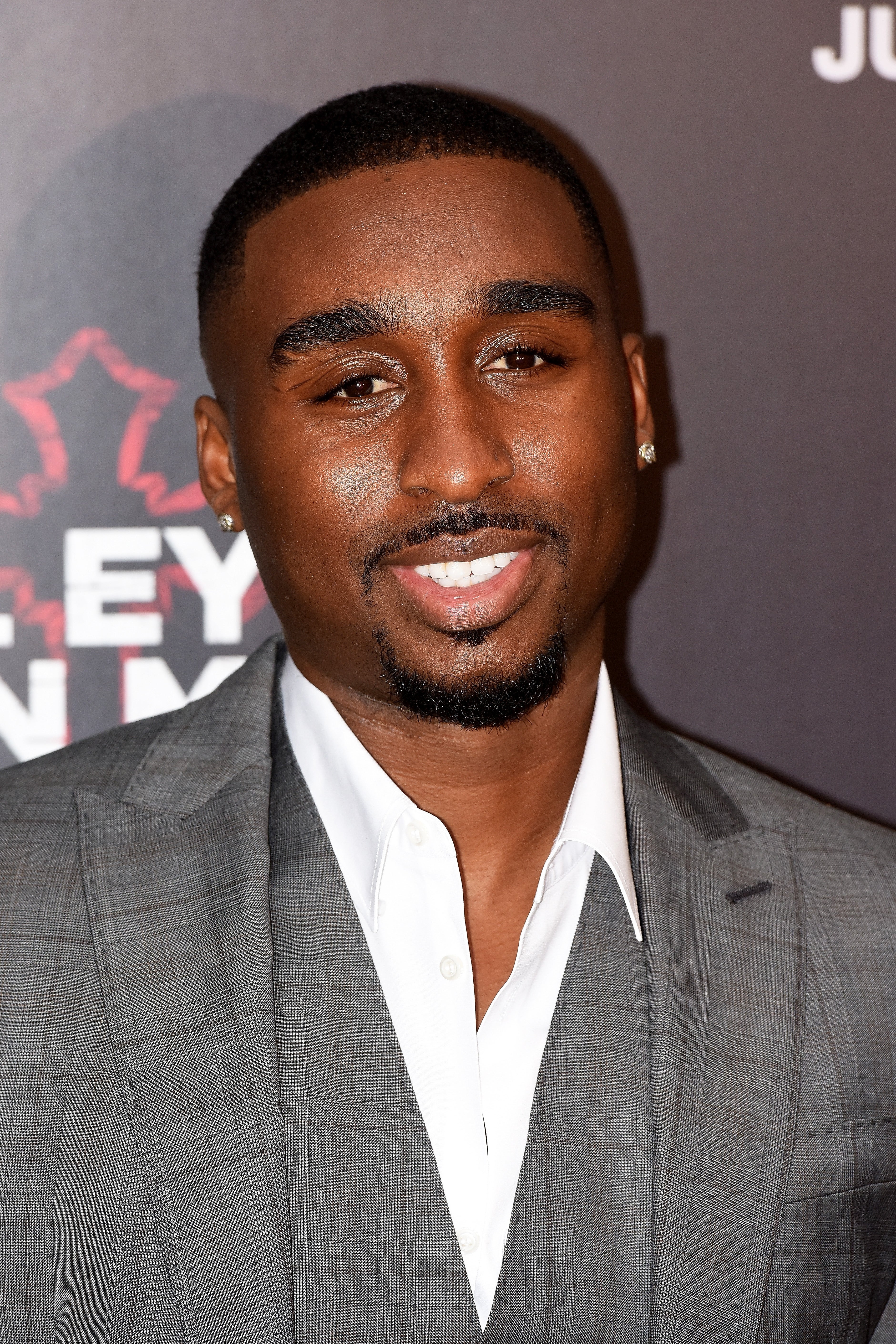 Demetrius Shipp Jr. in a sharp gray suit on the red carpet, smiling confidently at the camera