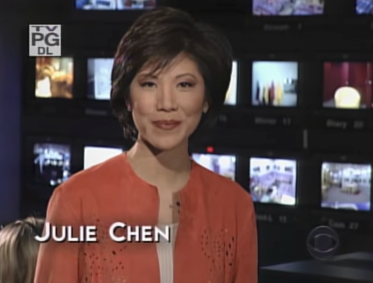 A person stands in front of multiple video screens, wearing a smart, casual outfit