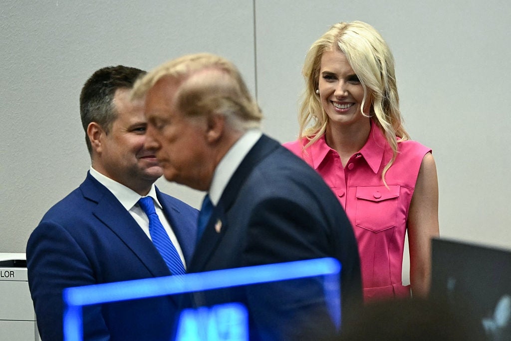 Tre personer i en konferansesetting, med en kvinne smilende i en rosa ermeløs bluse