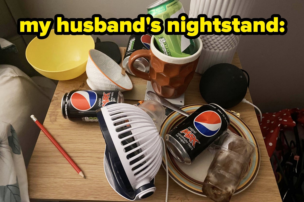 Cluttered nightstand with soda cans, a pencil, cups, bowls, and a massage device; rext reads: "my husband's nightstand"