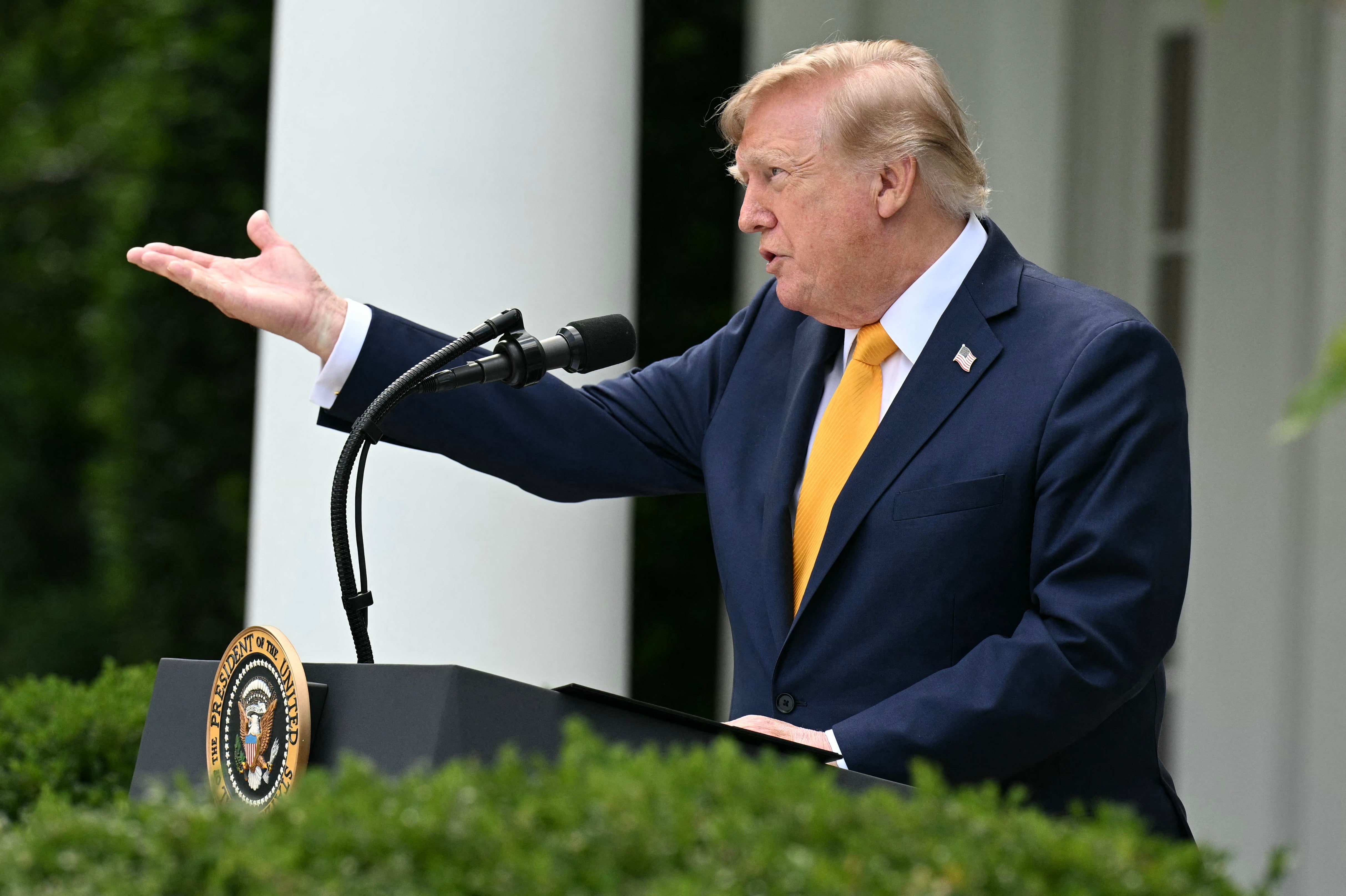 En mann i dress snakker ved et podium med en presidentsegl og gestikulerer med hånden